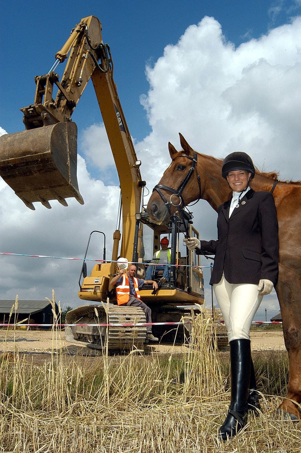 A digger breaks ground on a new equestrian centre, watched by a horse and rider.