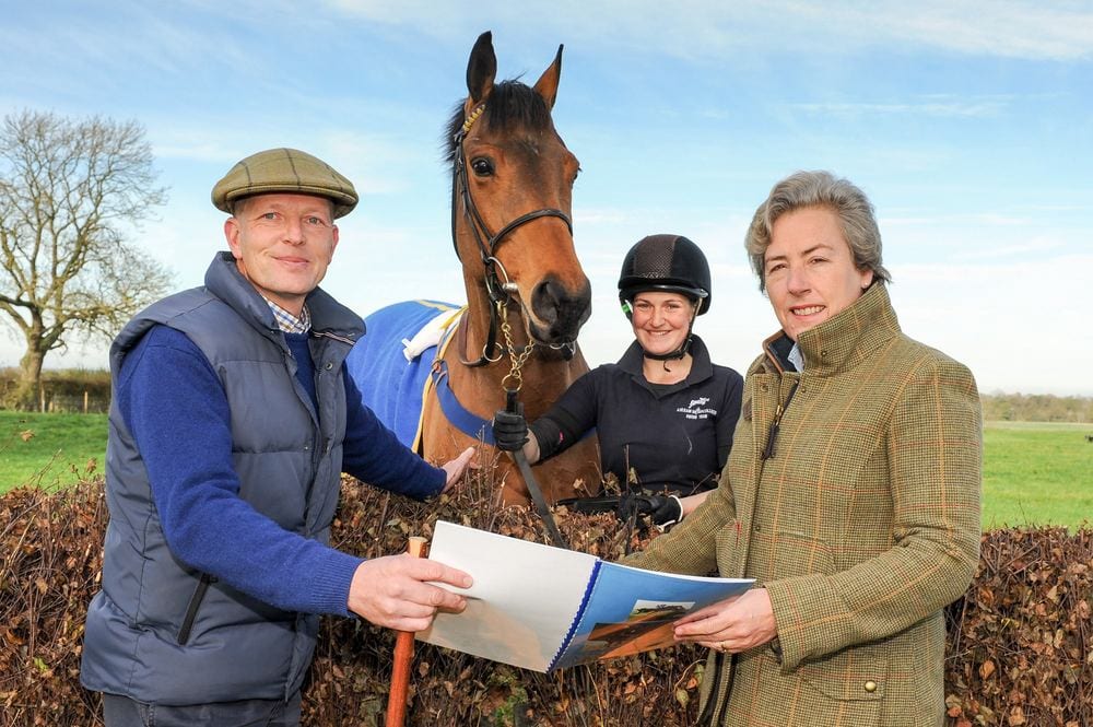 Equestrian plans held by two people, watched by a horse and rider.