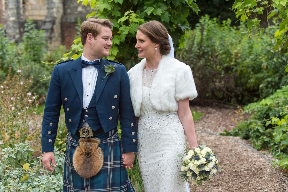 A newly married couple walk hand in hand through a garden.