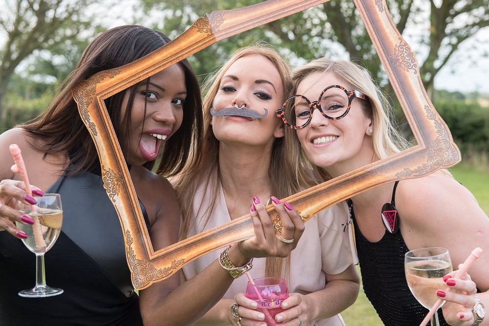 The hen party pose through a photo frame, in fake moustaches and glasses.