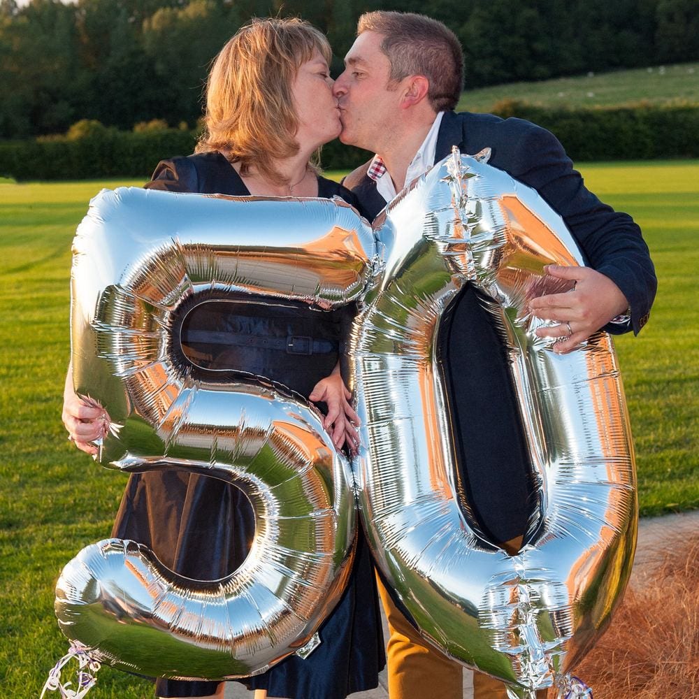 A couple kiss over a wall of 50 balloons.