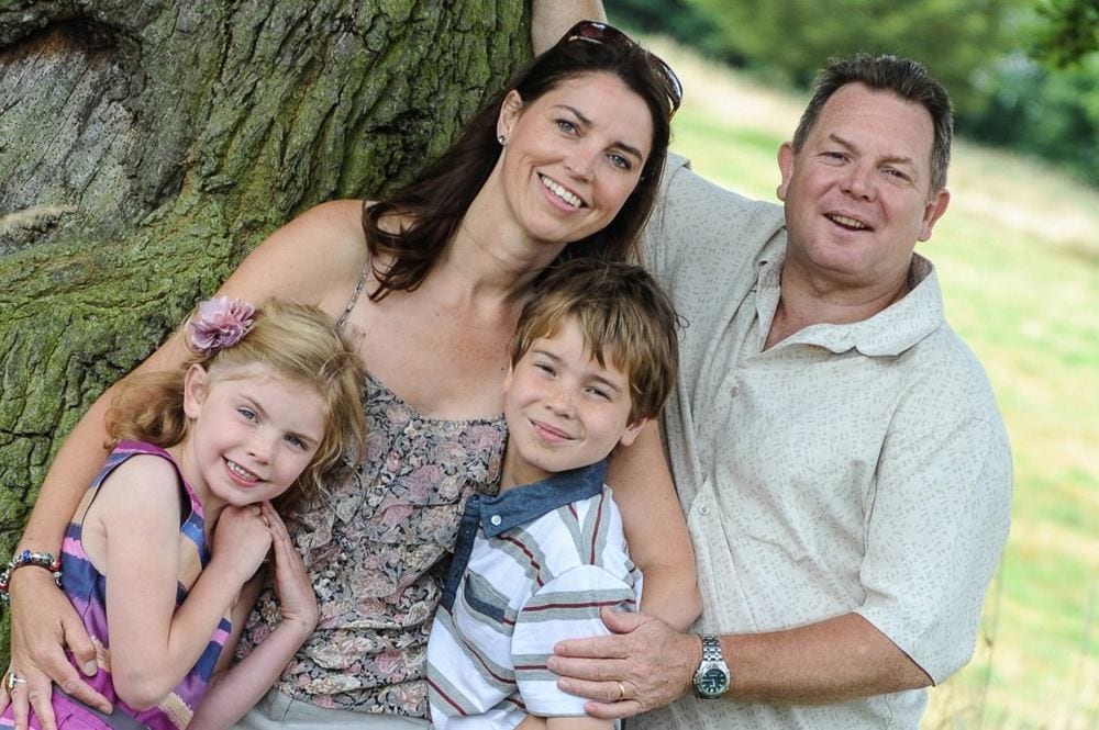 Parents with their son and daughter, leaning against a tree.
