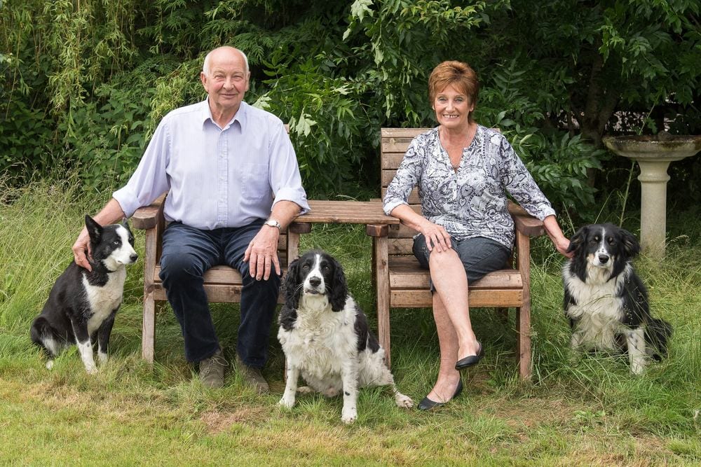 A couple sitting in their garden with their three dogs.