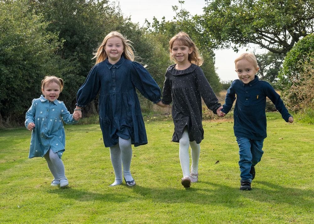 Four children holding hands, running toward the camera.