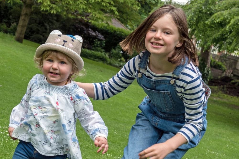 A sister chases her younger sister outdoors.