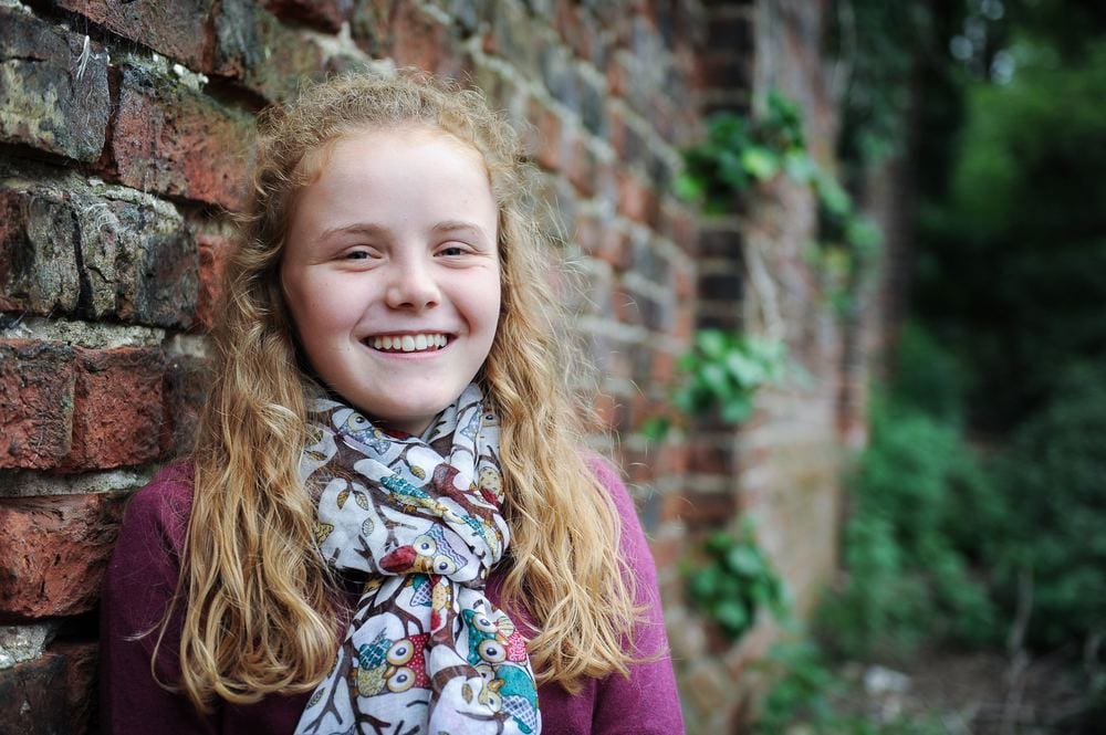 A young girl leans against an old brick wall.