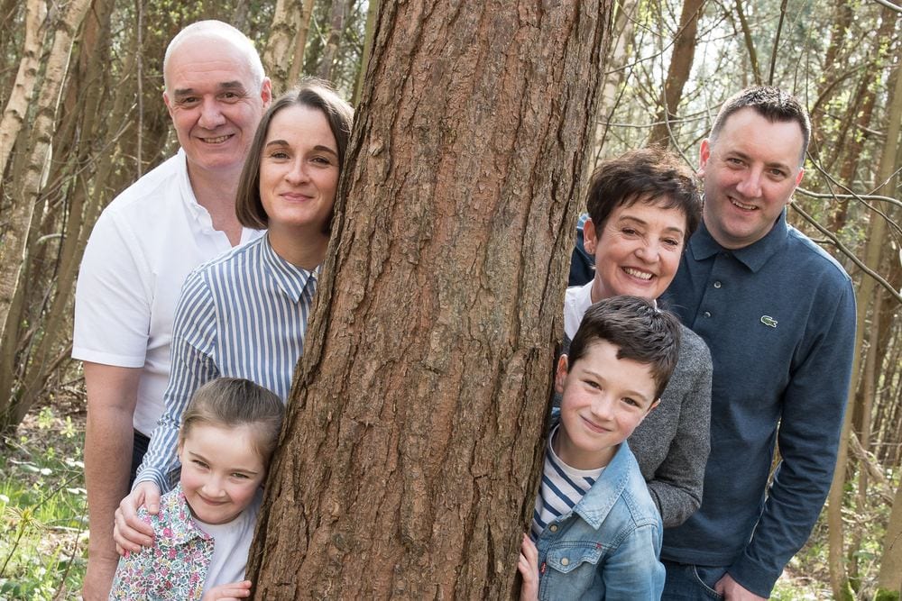 A family of four with two grandparents, peeking round a tree.